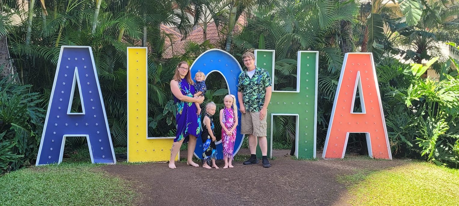 Family photo in front of "Aloha" sign in Honolulu, HI